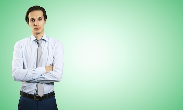 Business success concept with young smiling businessman folding his hands in white shirt and dark blue trousers on abstract light green blank background with place for your logo or text Mock up