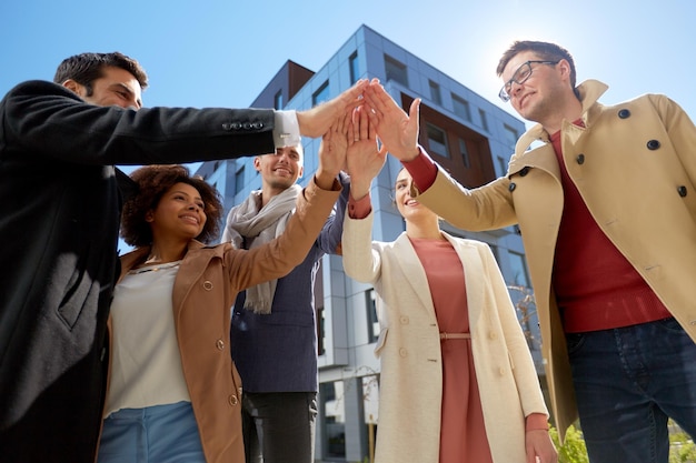 business, success and gesture concept - international group of people or students making high five on city street