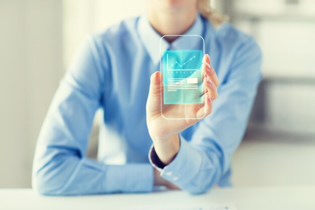 Photo business, success, statistics, technology and people concept - close up of woman hand holding and showing transparent smartphone with chart at office