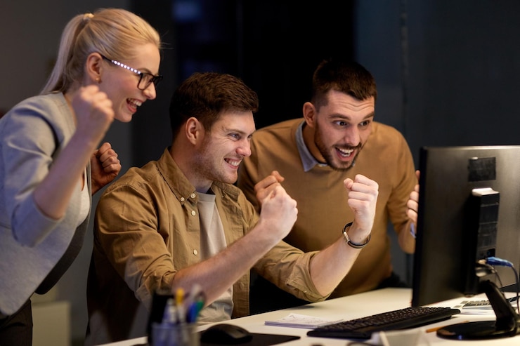 Photo business success and teamwork concept happy coworkers with computer celebrating victory at night office