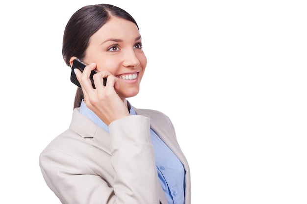 Business talk. Beautiful young businesswoman talking on the mobile phone and smiling while standing against white background