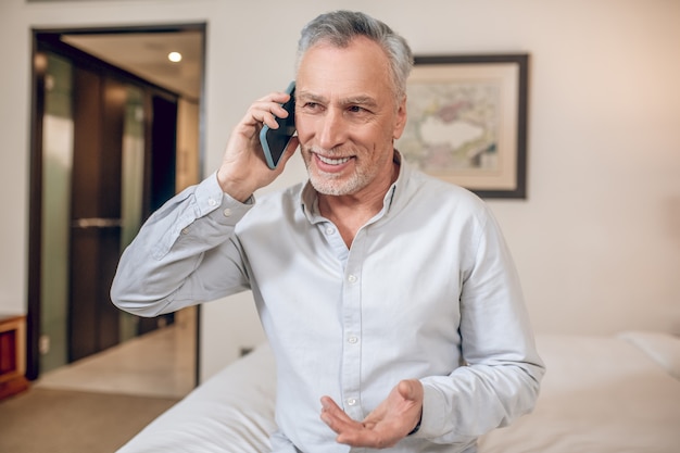 Business talk. Mid-aged gray-haired businessman talking on the phone and looking involved