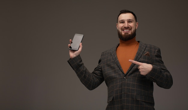 Business talk. Smiling young bearded man in suit using smart phone. Isolated on grey.