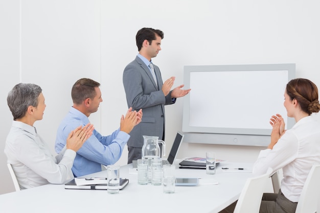 Business team applauding and looking at white screen