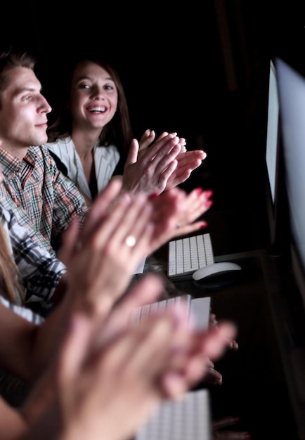 Business team applauding while sitting in front of computer screens