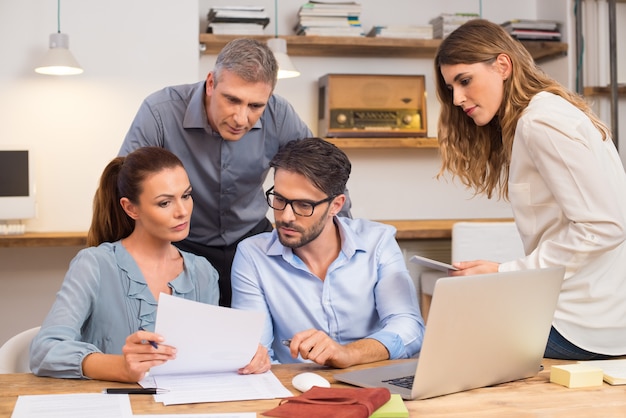 Business team bespreken op document en idee tijdens vergadering. Ondernemers kijken naar de geschiedenis van een bedrijf voor fusie. Ontmoeting op kantoor tussen creatieve mensen, informele zaken.