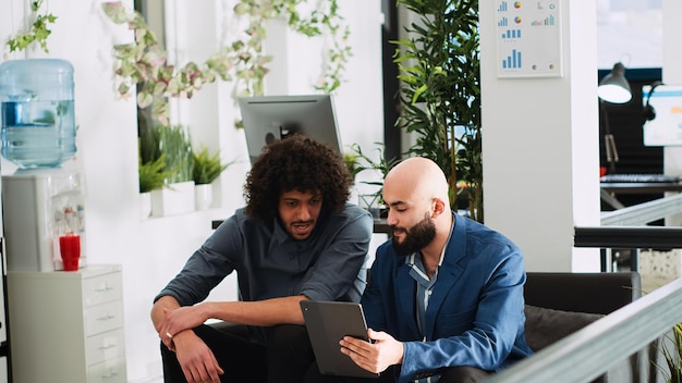 Business team examining reports on tablet, working on collaboration to increase profit for startup. Office workers doing teamwork in boardroom open space, planning development project.