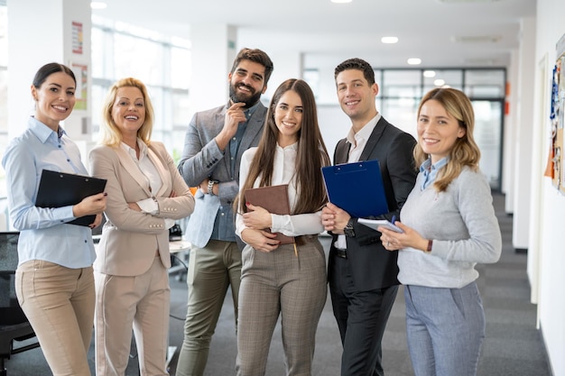 Business team Group portrait of happy motivated employees colleagues standing in modern office holding gadgets documents and looking at camera
