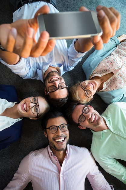 Business team lying on the floor with head together and taking selfie