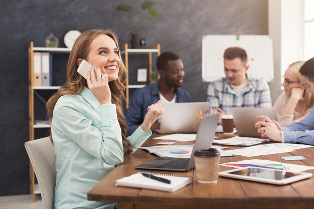 Business team praten over de resultaten van hun werk. Groep vrolijke zakenmensen die nieuwe marketingstrategie bespreken, jonge vrouw die telefonisch praat, ruimte kopieert