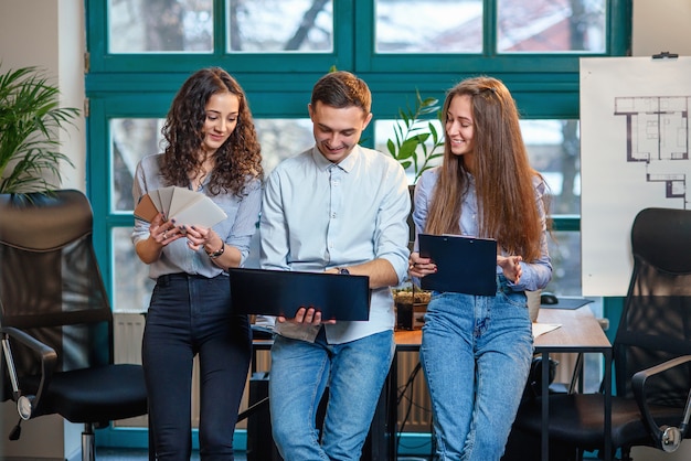 Squadra di affari di giovani architetti o designer che creano nuovo progetto mentre lavorano nell'ufficio moderno ed elegante con una grande finestra.