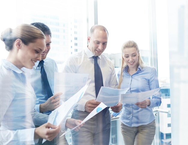 ビジネス、チームワーク、人と技術の概念-オフィスで会議を行う書類を持つ笑顔のビジネスチーム