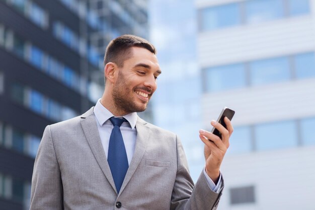 business, technologie en mensen concept - lachende zakenman met smartphone over kantoorgebouw