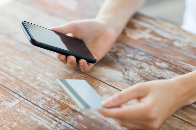 business, technology, cash free and internet people concept - close up of male hands holding smart phone and credit card on wooden table