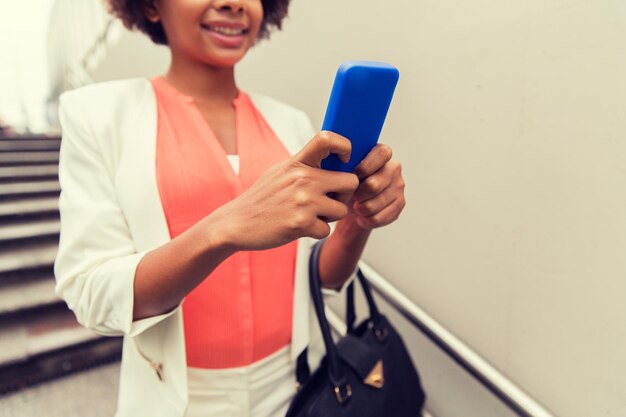 business, technology, communication and people concept - close up of young smiling african american businesswoman with smartphone and handbag texting walking downstairs to city subway