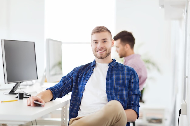 비즈니스, 기술, 커뮤니케이션 및 사람 개념 - 사무실에서 컴퓨터와 스마트폰을 사용하는 행복한 청년 또는 학생