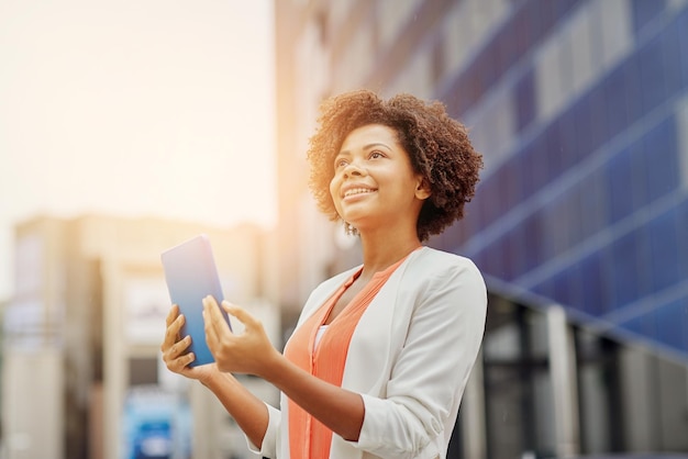 бизнес, технологии, общение и концепция людей - молодая улыбающаяся афроамериканская деловая женщина с планшетным компьютером в городе
