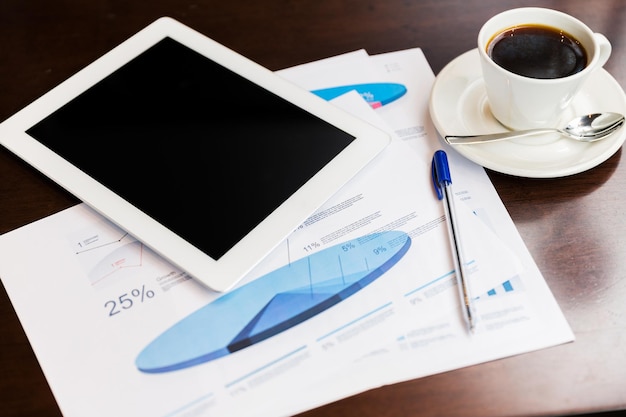 business and technology concept - close up of tablet pc computer, charts and coffee cup on table