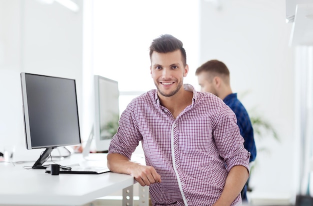 business, technology, education and people concept - happy young creative man or student with computer at office