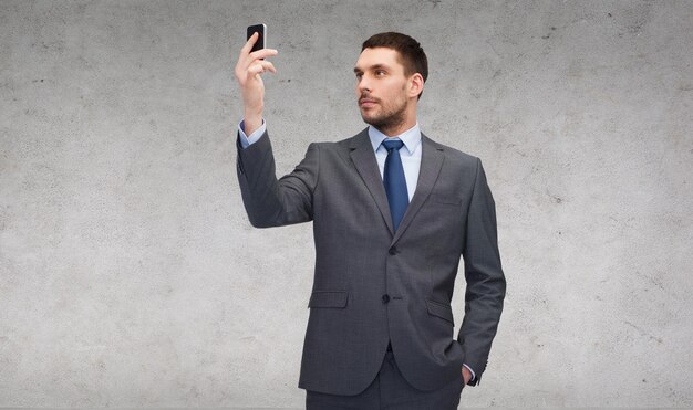 business, technology, internet and education concept - friendly young businessman with smartphone