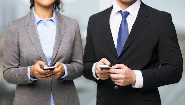 business, technology, internet and office concept - businessman and businesswoman with smartphones in office