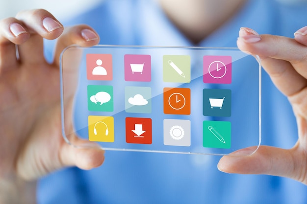 写真 ビジネス、テクノロジー、メディア、人々のコンセプト – 透明なスマートフォンを持ち、オフィスの画面にメニューアイコンを表示する女性の手の接写