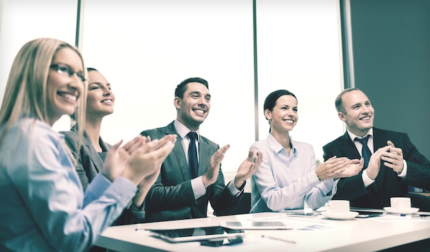 Concetto di business, tecnologia e ufficio - team aziendale felice con computer portatili, documenti e caffè che applaudono la mano