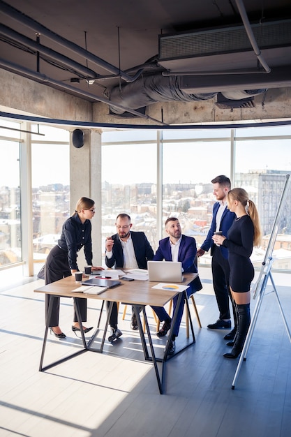 Business, technology and office concept - happy business team with laptop computers, documents and coffee. Meeting before the start of the working day to discuss a business plan