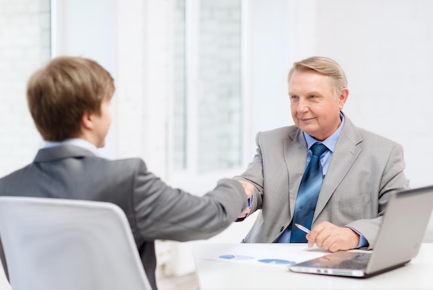 ビジネス、テクノロジー、オフィスのコンセプト-オフィスで握手する年配の男性と若い男性
