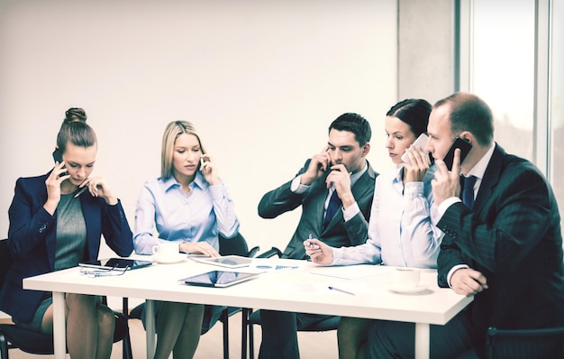 business, technology and office concept - serious business team with smartphones making calls in office