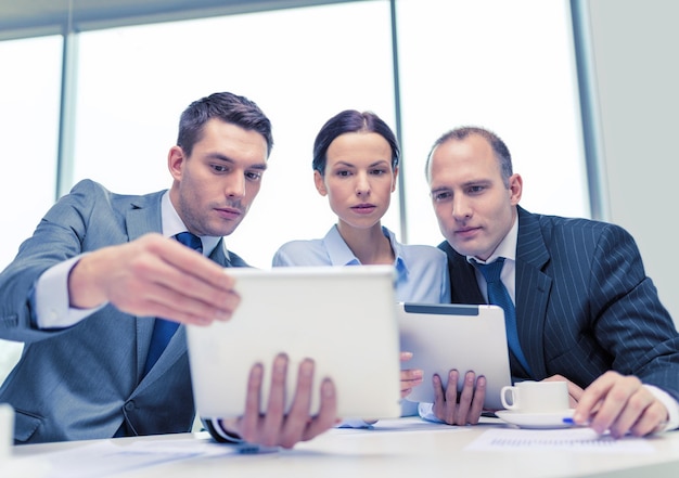 business, technology and office concept - serious business team with tablet pc computers, documents and coffee having discussion in office