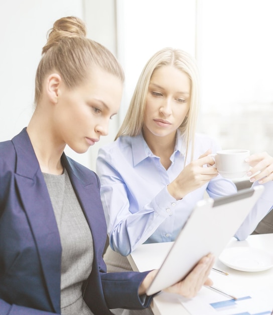 business, technology and office concept - serious businesswomen with tablet pc computers having discussion in office