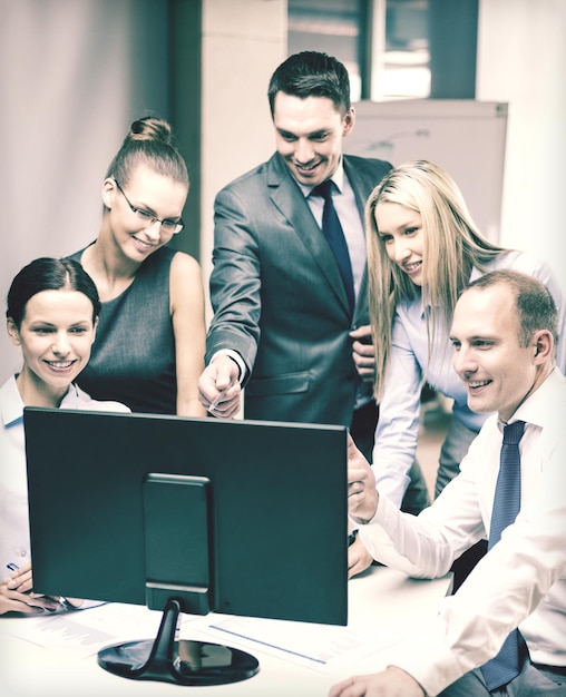 business, technology and office concept - smiling business team with computer monitor having discussion in office