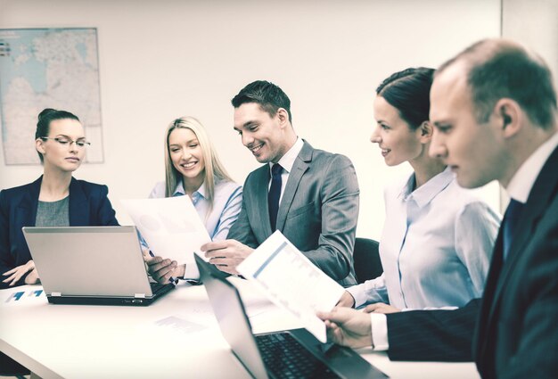 business, technology and office concept - smiling business team with laptop computers and documents having discussion in office