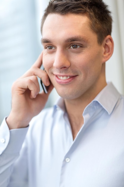 business, technology and office concept - smiling businessman with smartphone in office