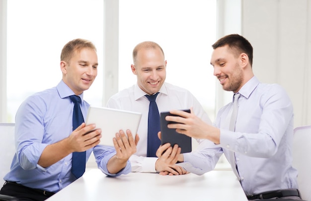 business, technology and office concept - three smiling businessmen with tablet pc computers in office