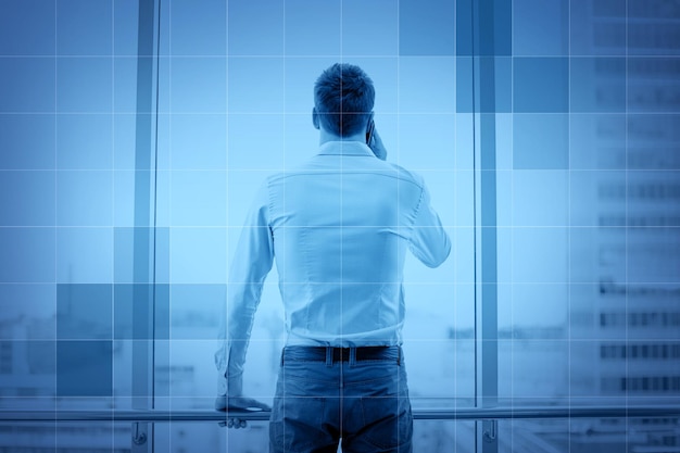 business, technology and people concept - businessman calling on smartphone and looking out office window behind monochrome blue grid