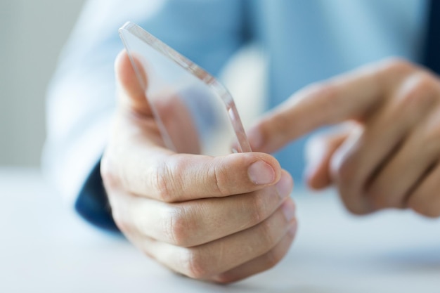 business, technology and people concept - close up of male hand holding and showing transparent smartphone at office