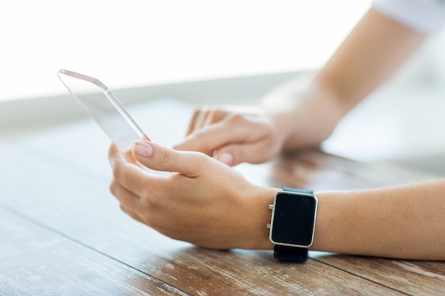 business, technology and people concept - close up of woman hand holding and showing transparent smart phone and watch at office