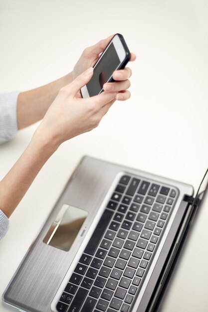 business, technology and people concept - close up of woman hands with laptop computer and smartphone texting message at office