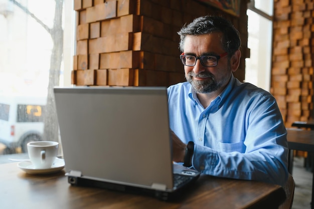 Foto tecnologia aziendale e concetto di persone uomo d'affari senior con computer portatile che beve caffè al caffè moderno