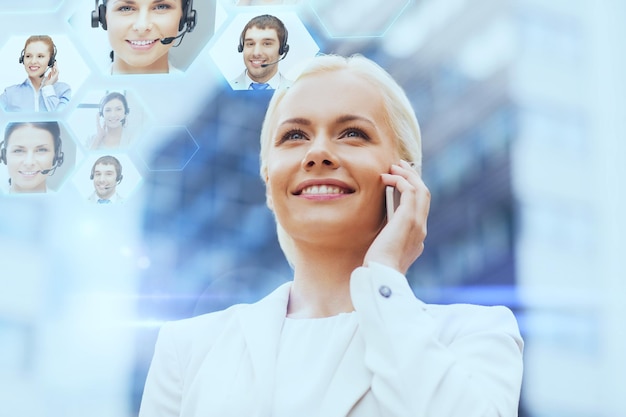 business, technology and people concept - smiling businesswoman with smartphone calling to helpline over office building