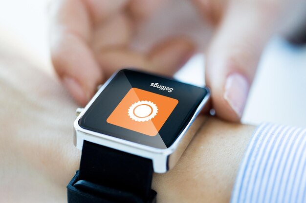 business, technology, settings and people concept - close up of woman hands with cogwheel icon on smartwatch screen