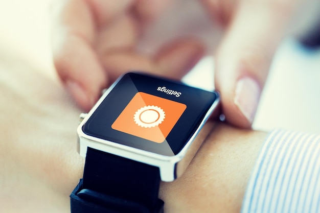 business, technology, settings and people concept - close up of woman hands with cogwheel icon on smartwatch screen