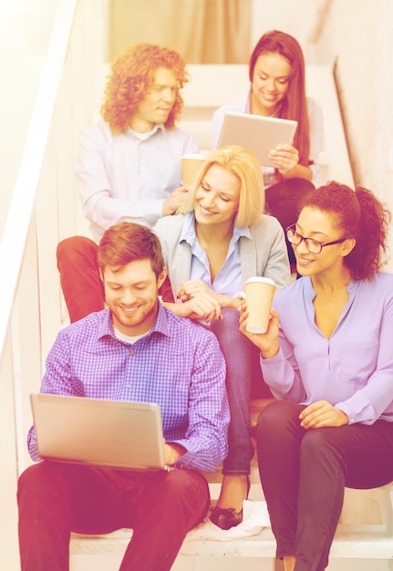 концепция бизнеса, технологий и запуска - улыбающаяся творческая команда с ноутбуком и планшетным компьютером, сидящая на лестнице