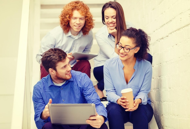 business, technology and startup concept - smiling creative team with laptop and tablet pc computer sitting on staircase