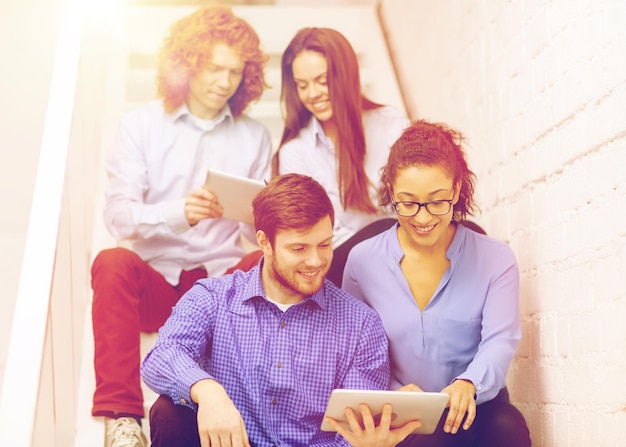 business, technology and startup concept - smiling creative team with tablet pc computer sitting on staircase