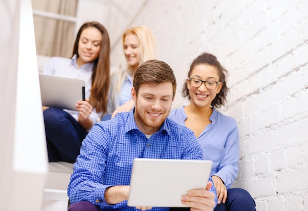 business, technology and startup concept - smiling creative team with tablet pc computer sitting on staircase