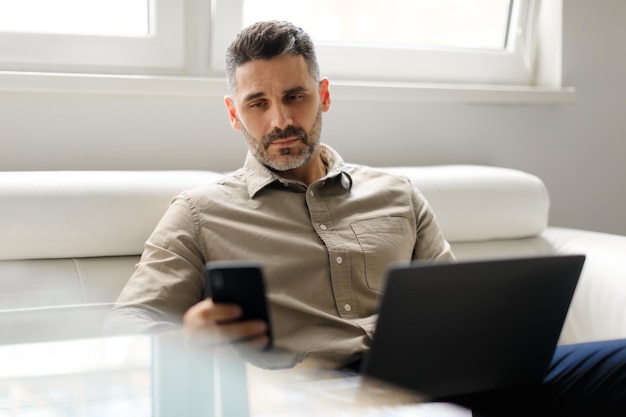 Business and telecommuting concept middle aged businessman using smartphone sitting on sofa in