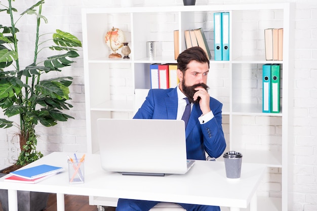 Business thinking Serious businessman sit at office desk Bearded men think over serious business Project manager with serious look Work and career Professional life Serious and thoughtful